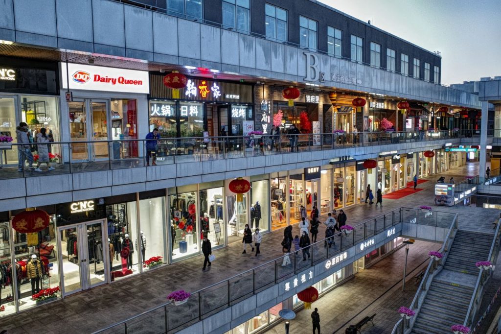 Bustling evening at a modern shopping mall with various shops and pedestrians.